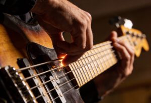Nahaufnahme einer Hand beim Slap-Bass-Spiel auf einer E-Bass-Gitarre, Fokus auf Saiten, Pickup und Slap-Technik.