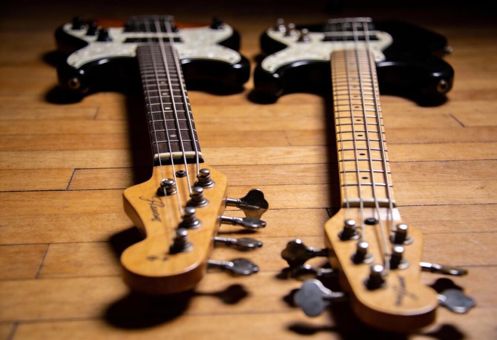 Zwei verschiedene Bassgitarren liegen parallel auf einem Holzboden.
