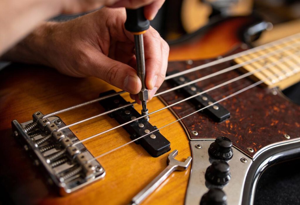 Detailaufnahme einer Hand, die mit einem Schraubenzieher die Stegeinstellungen einer Bassgitarre anpasst.