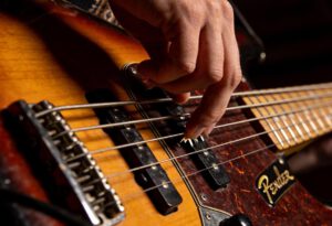 Ein Musiker spielt mit einer Hand auf einem Bassguitar und nutzt ein Plektrum.