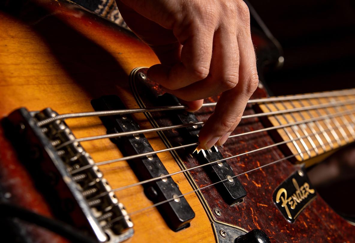 Ein Musiker spielt mit einer Hand auf einem Bassguitar und nutzt ein Plektrum.