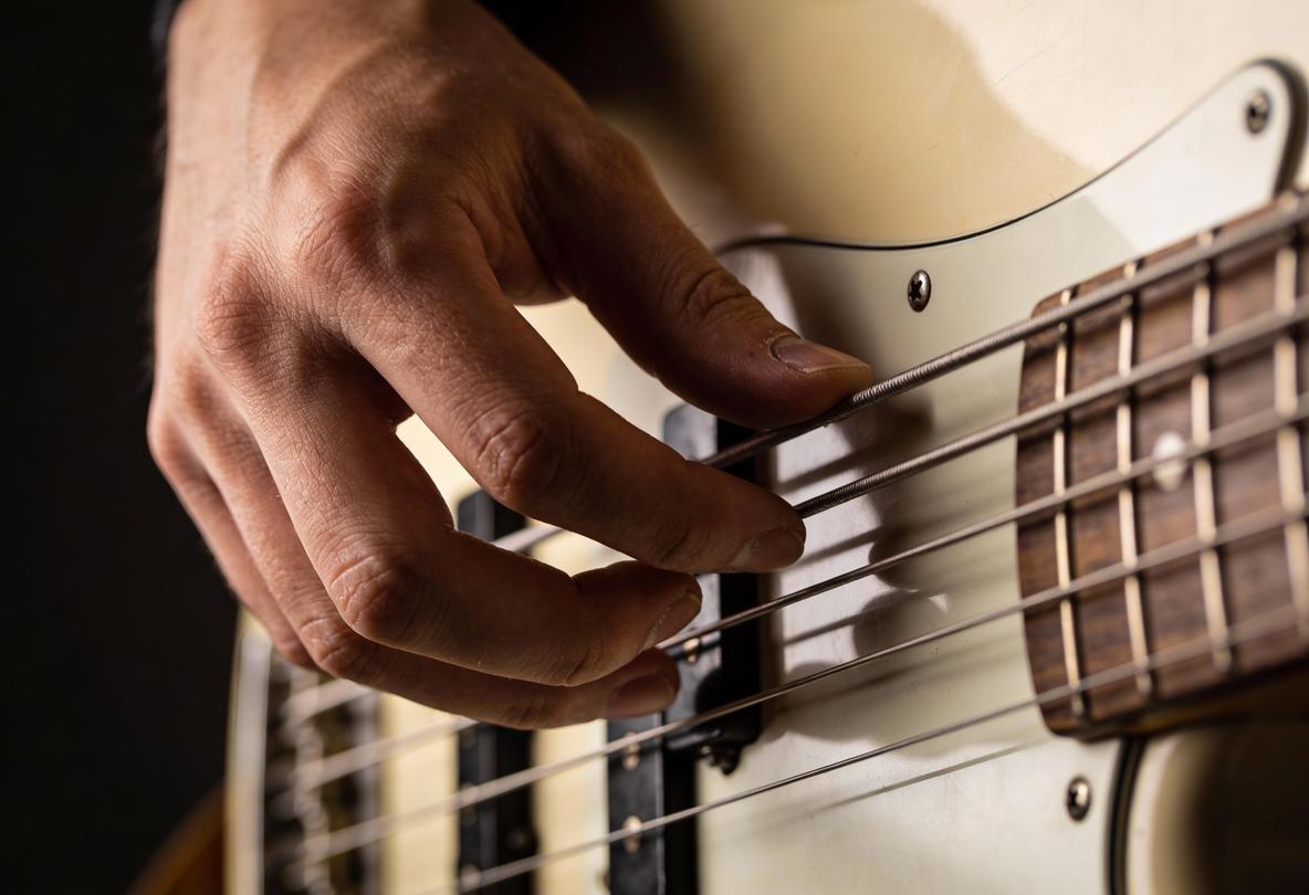 Nahaufnahme einer Hand, die die Saiten eines Basses spielt.