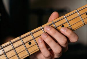 Hand spielt auf den Saiten einer E-Bassgitarre