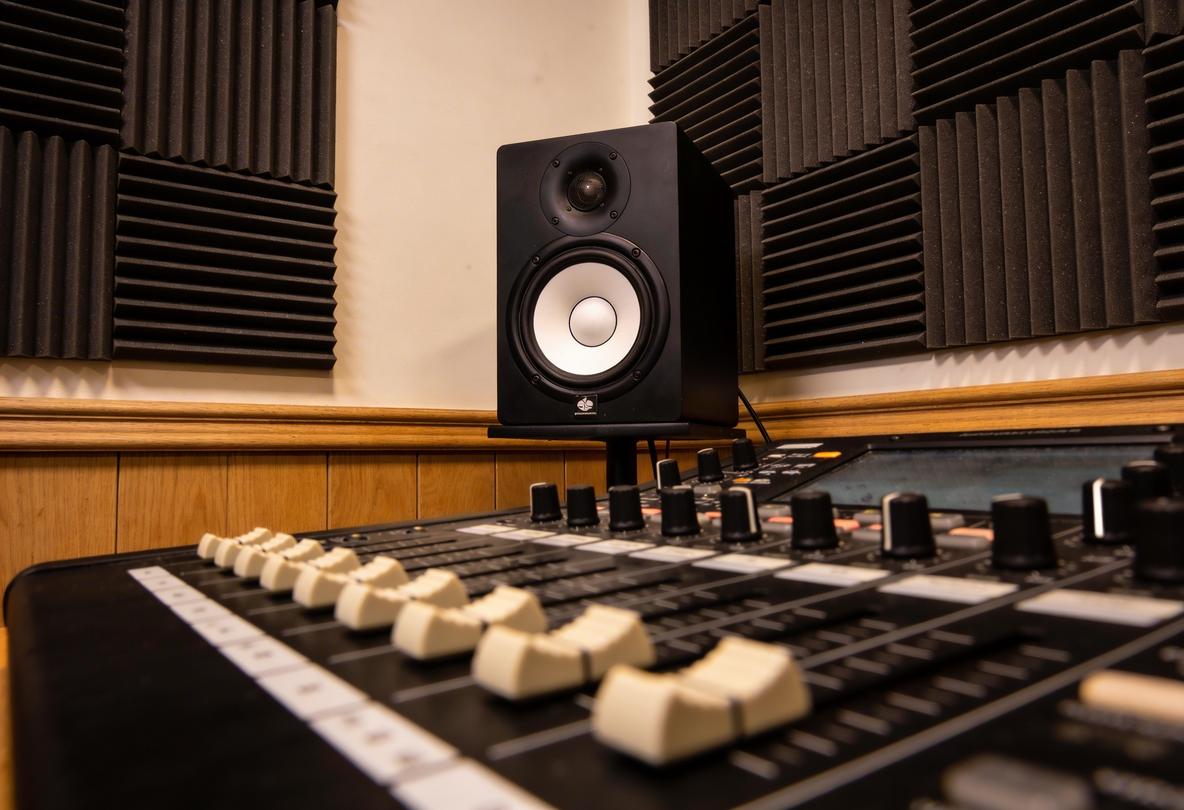 Nahaufnahme eines Studiomischpults mit Lautsprecher im Hintergrund