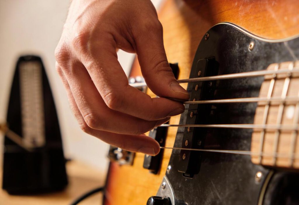 Nahaufnahme einer Hand, die eine Bassgitarre spielt, mit einem Metronom im Hintergrund.
