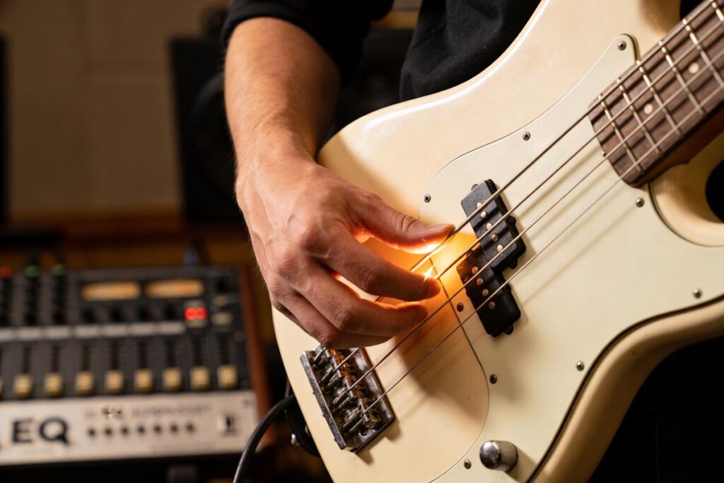 Nahaufnahme einer Hand, die die Saiten eines E-Basses spielt, mit einer Lichtquelle, die den Bereich beleuchtet.