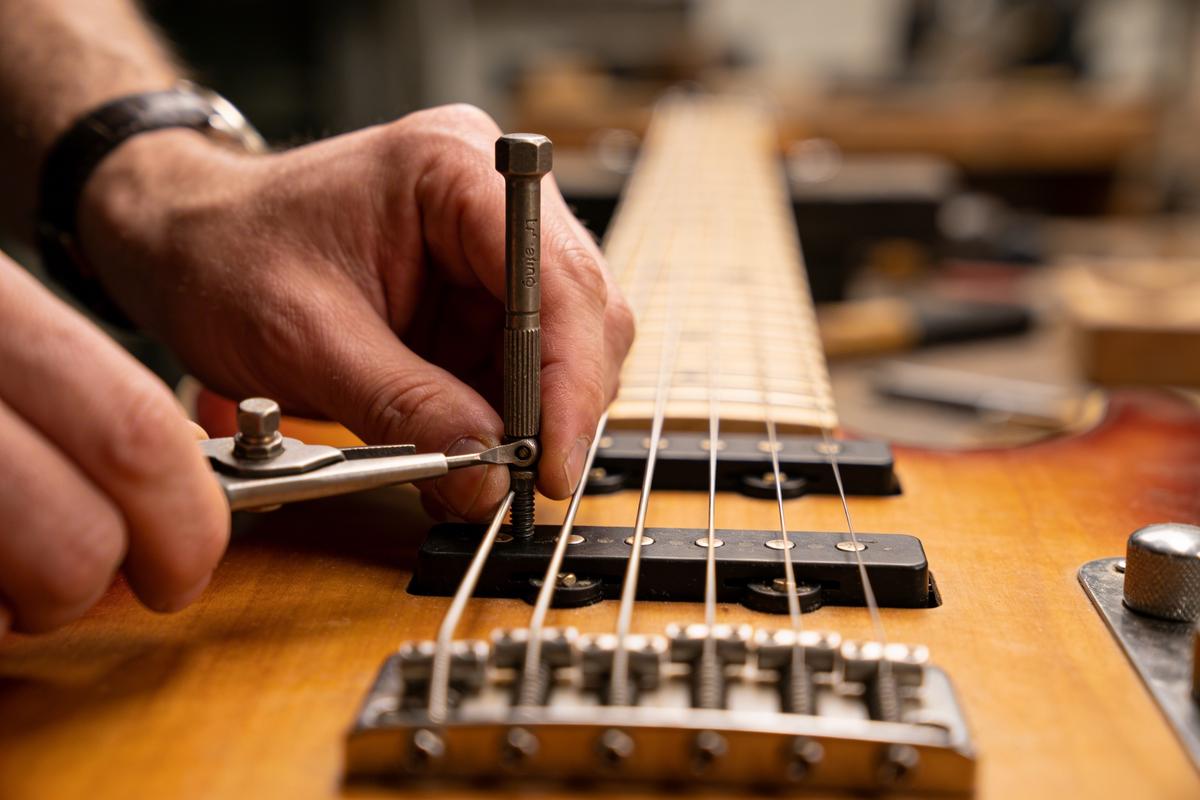 Eine Hand verwendet Werkzeuge zur Justierung einer Bassgitarre