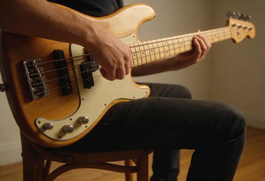 Ein Bassist spielt einen E-Bass auf einem Stuhl.
