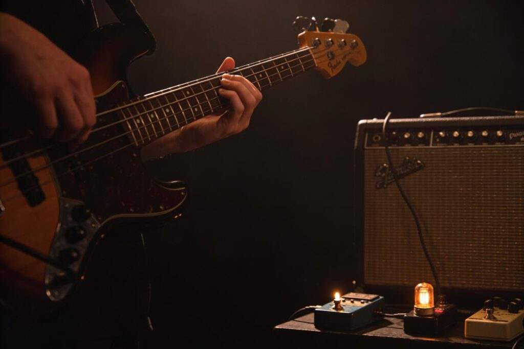 Der Arm eines Bassisten spielend auf einem E-Bass neben Effektpedalen und Verstärker.