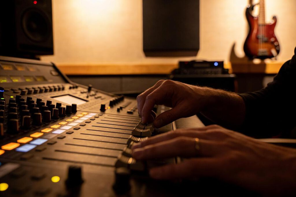 Hände eines Bassisten, die an einem Mischpult im Tonstudio arbeiten