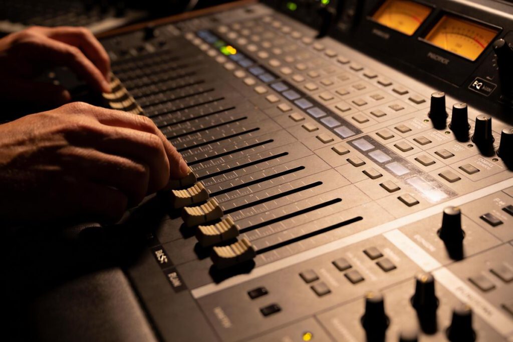 Hände bedienen einen Mischpult-Regler in einem Studio