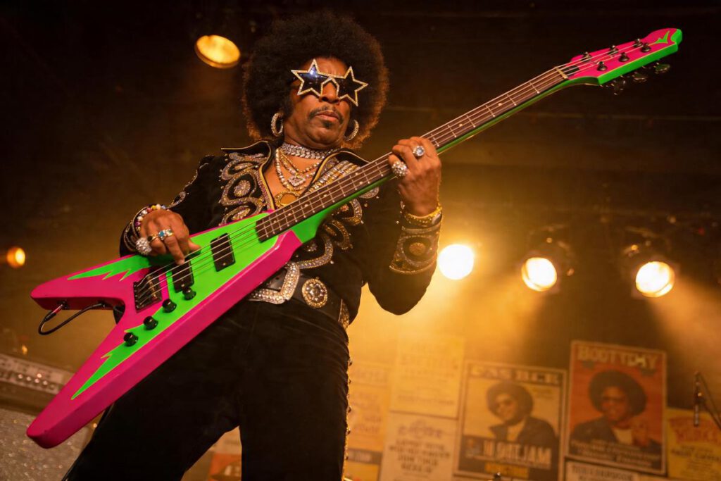 Ein Bassist spielt eine leuchtend grüne und pinke E-Gitarre während eines Konzerts.