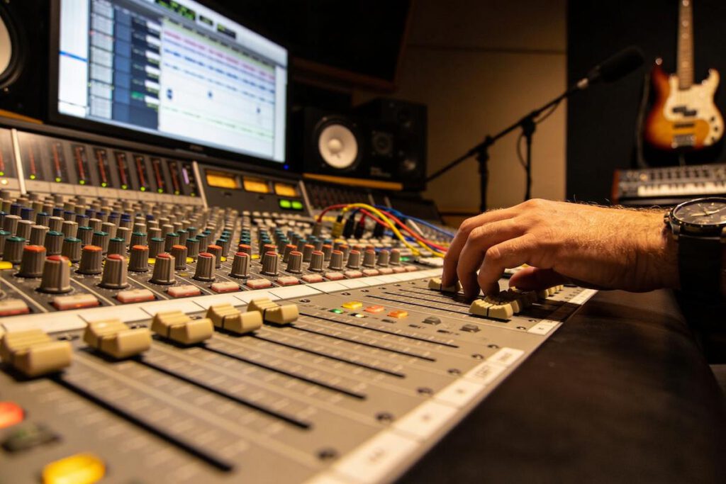 Nahaufnahme einer Mixing-Konsole mit Reglern und Hand eines Toningenieurs