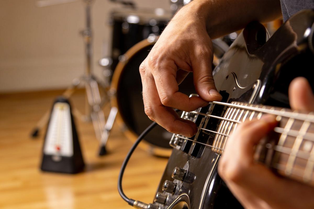 Nahaufnahme einer Hand, die auf den Saiten eines Basses spielt, im Hintergrund eine Trommel.