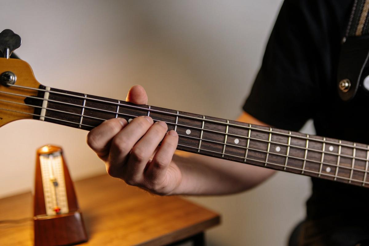 Ein Bassist spielt auf einer Bassgitarre, während ein Metronom im Hintergrund leuchtet.