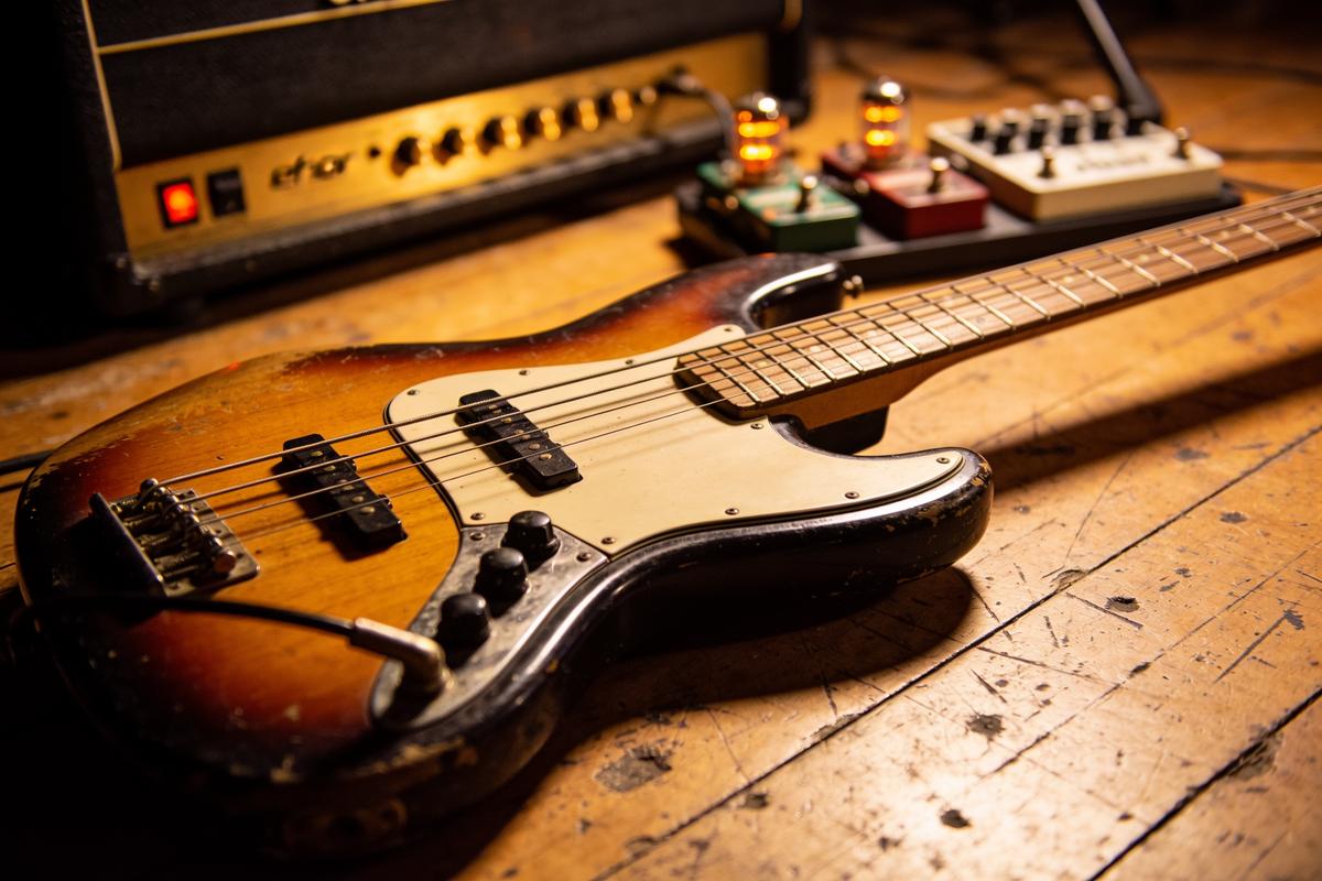 Ein vintage Bassgitarre liegt auf einem Holzboden neben einem Verstärker und Effektpedalen.