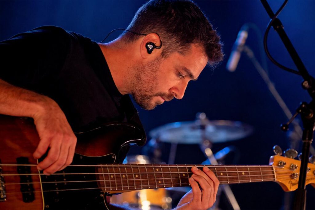 Ein Bassist, der konzentriert auf seinem Instrument spielt, mit einem Mikrofon in der Nähe.