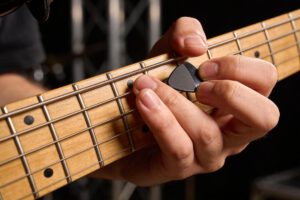 Näheraufnahme einer Hand, die ein Plektrum auf einer Bassgitarre benutzt.