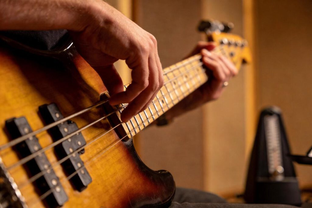 Nahaufnahme eines Bassisten, der mit der rechten Hand die Saiten eines E-Basses zupft.